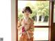 A woman in a kimono standing in front of a window.