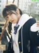 A young woman in a school uniform leaning against a fence.