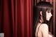 A woman with long black hair standing in front of a curtain.