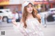 A woman in a white dress and a baseball cap is walking down the street.