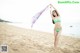 A woman in a green bikini holding a scarf on the beach.